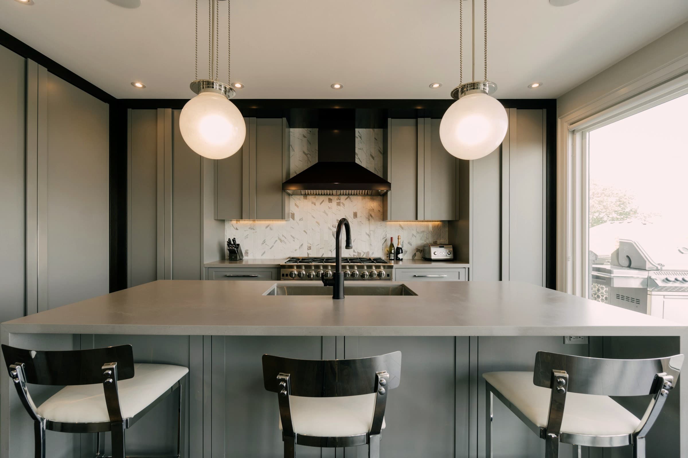 Dark green modular kitchen with a stone island and glass globe pendant lights